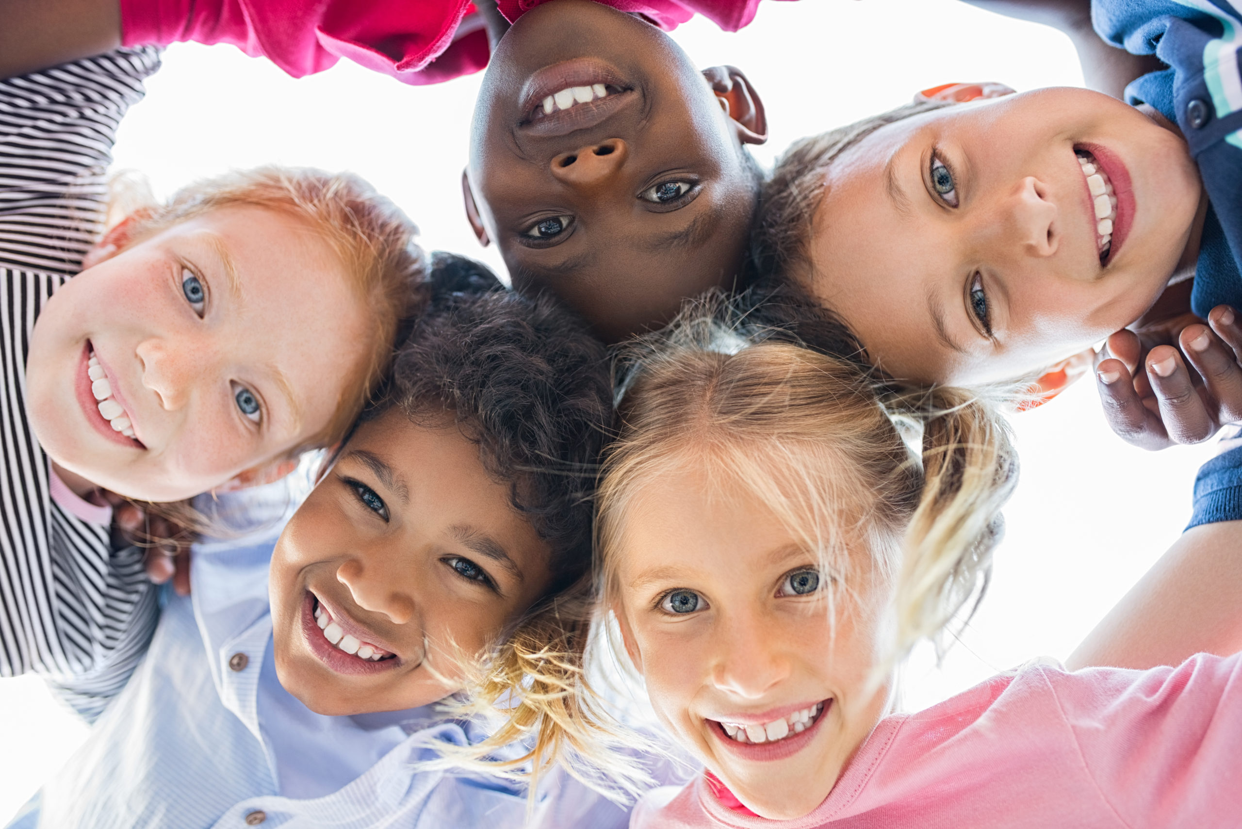 Multiethnic children in a circle Closeup face of happy multiethnic children embracing each other and smiling at camera. Team of smiling kids embracing together in a circle. Portrait of young boy and pretty girls looking at camera.