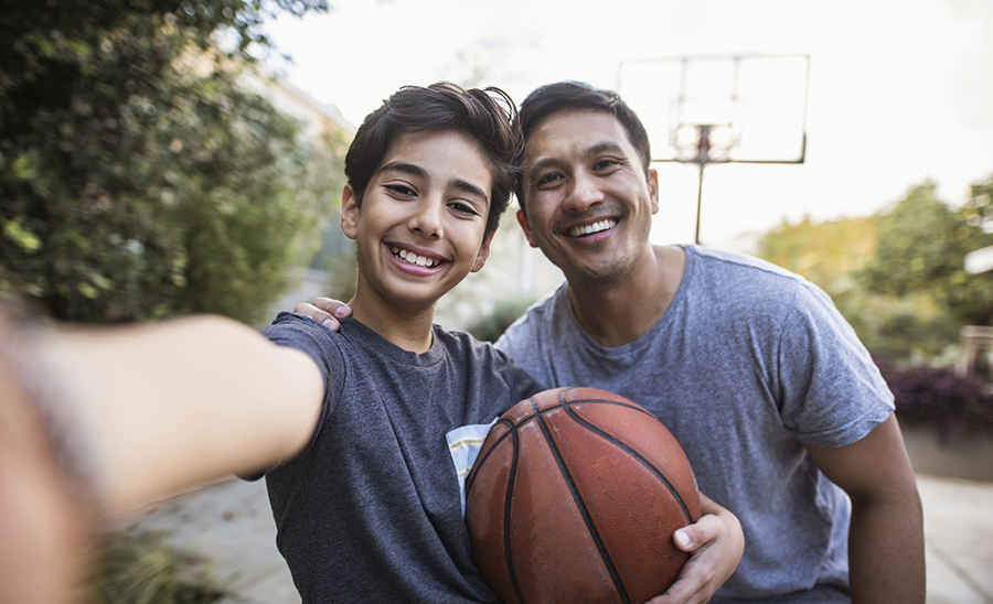 Hispanic father and son taking a selfie outdoors whilst playing basketball Hispanic father and son taking a selfie outdoors whilst playing basketball